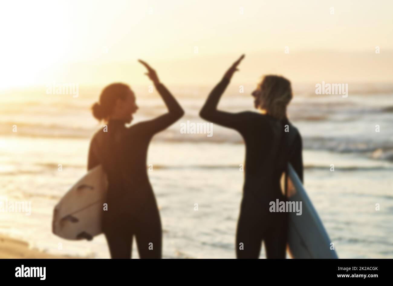 Hautes marées et hautes marées. Vue arrière d'un jeune couple se joignant à la main pour un haut cinq tout en surfant à la plage. Banque D'Images