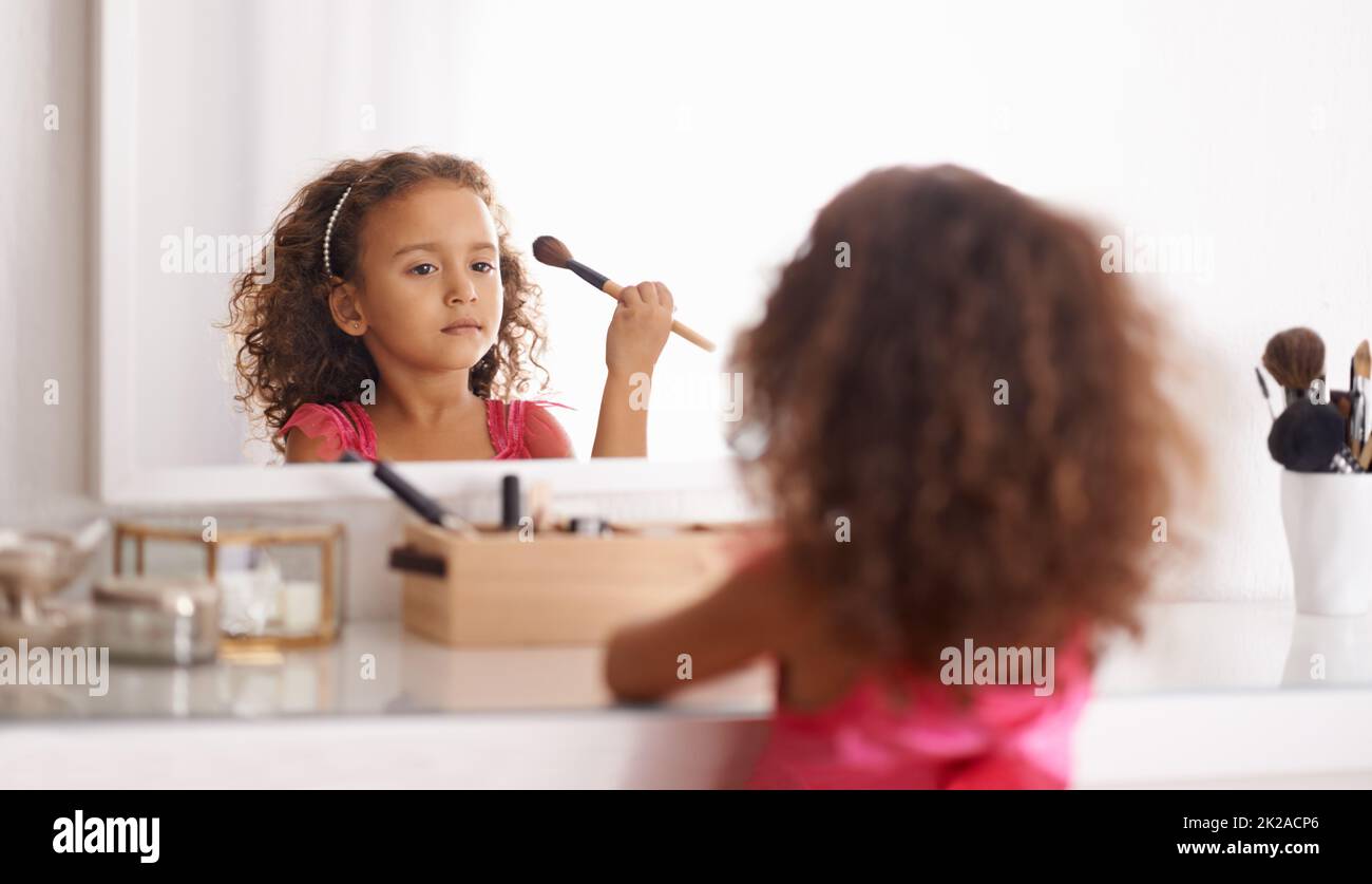 Je vais ressembler à ma maman. Photo d'une petite fille appliquant un fard à joues dans le miroir. Banque D'Images