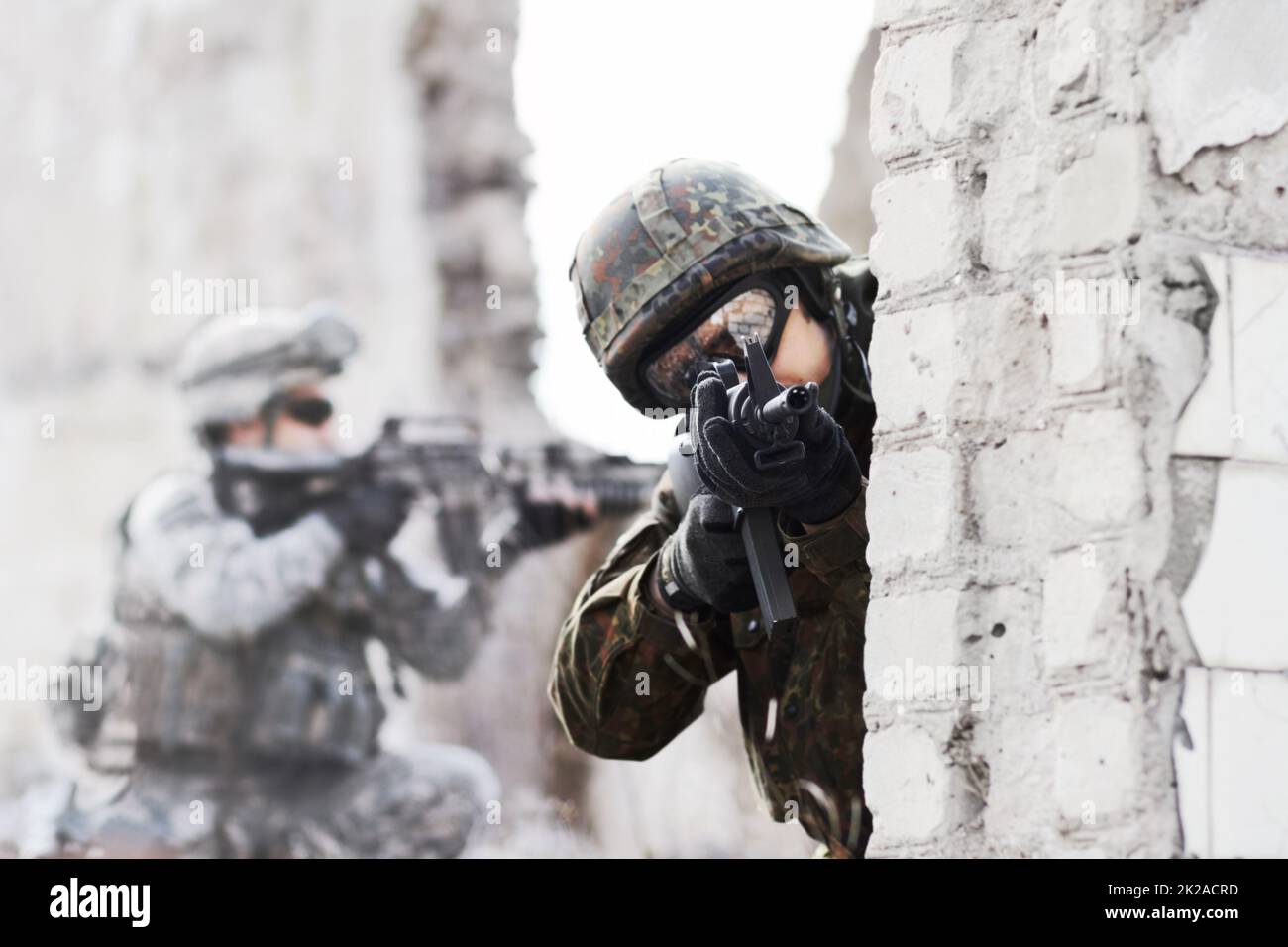 Force de défense dynamique. Un soldat qui se tourne autour d'un mur tout en pointant une arme à feu vers la caméra lors d'une rade sur un bâtiment endommagé. Banque D'Images