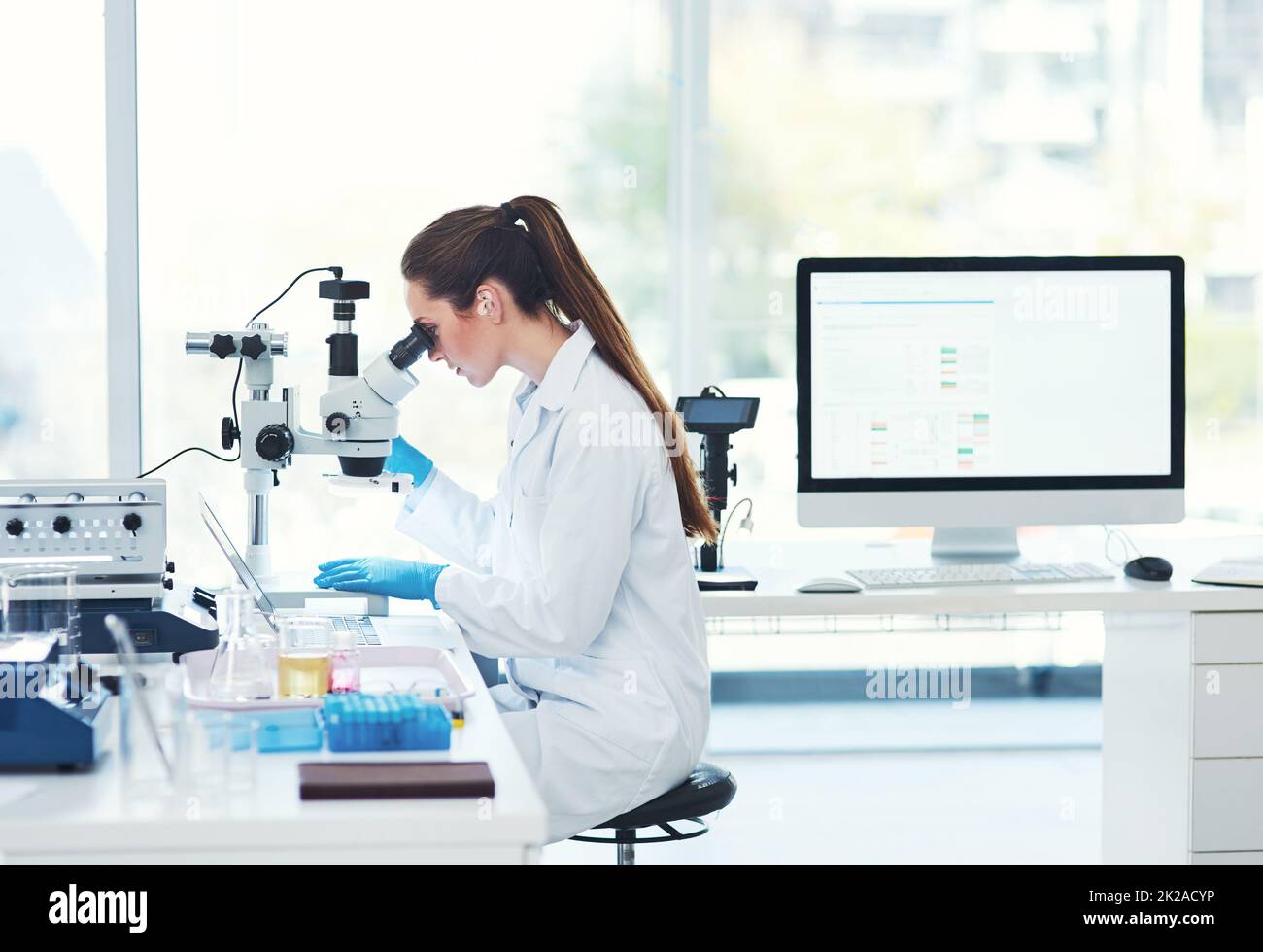 Tout cela en une journée de travail. Plan rogné d'une jeune scientifique ciblée regardant à travers un microscope tout en faisant des tests à l'intérieur d'un laboratoire. Banque D'Images