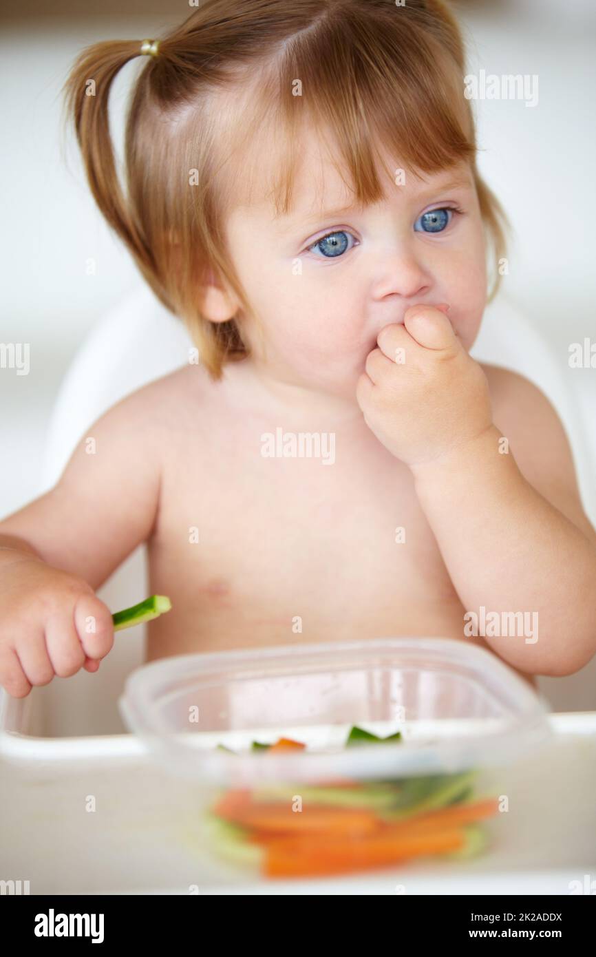 Les légumes sont très jeunes. Une petite fille mignonne qui mange des légumes. Banque D'Images