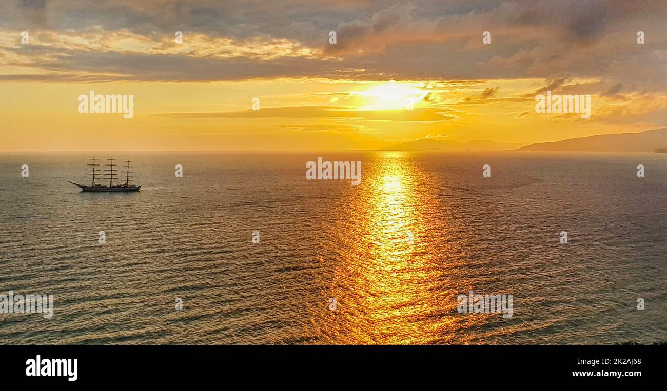 Romantique coucher de soleil doré sur la mer avec un yacht sur le fond des montagnes et des nuages orange, une scène calme d'une chaude soirée paisible Banque D'Images