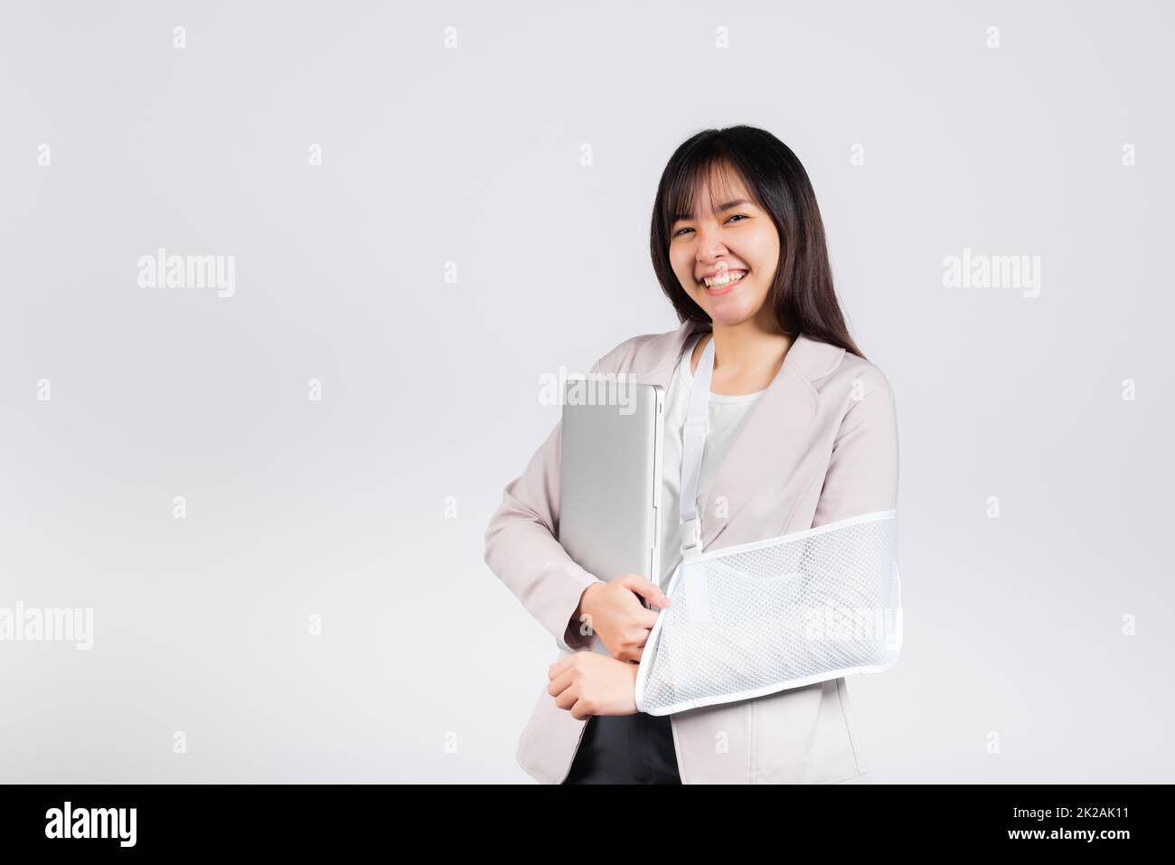 Femme d'affaires asiatique confiante souriante bras cassé après accident et porter une attelle de bras pour le traitement mais elle doit encore travailler elle tient un ordinateur portable Banque D'Images