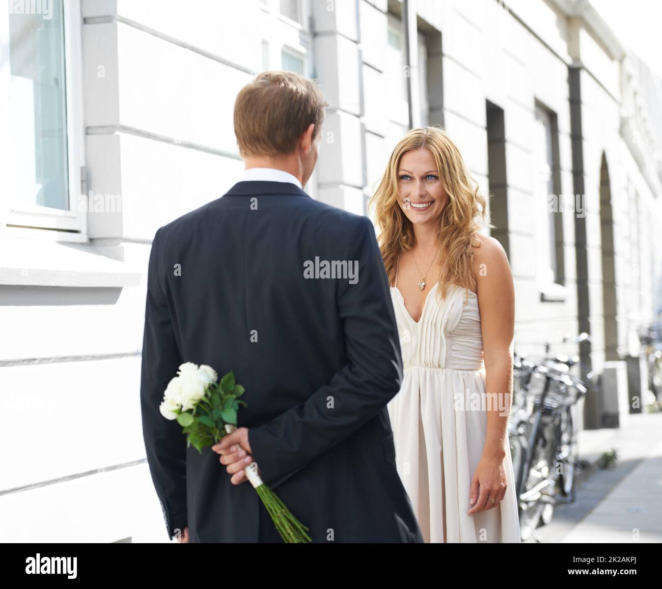 HES un tel tease. Une belle femme sourit à son petit ami tenant un bouquet de roses blanches derrière son dos. Banque D'Images