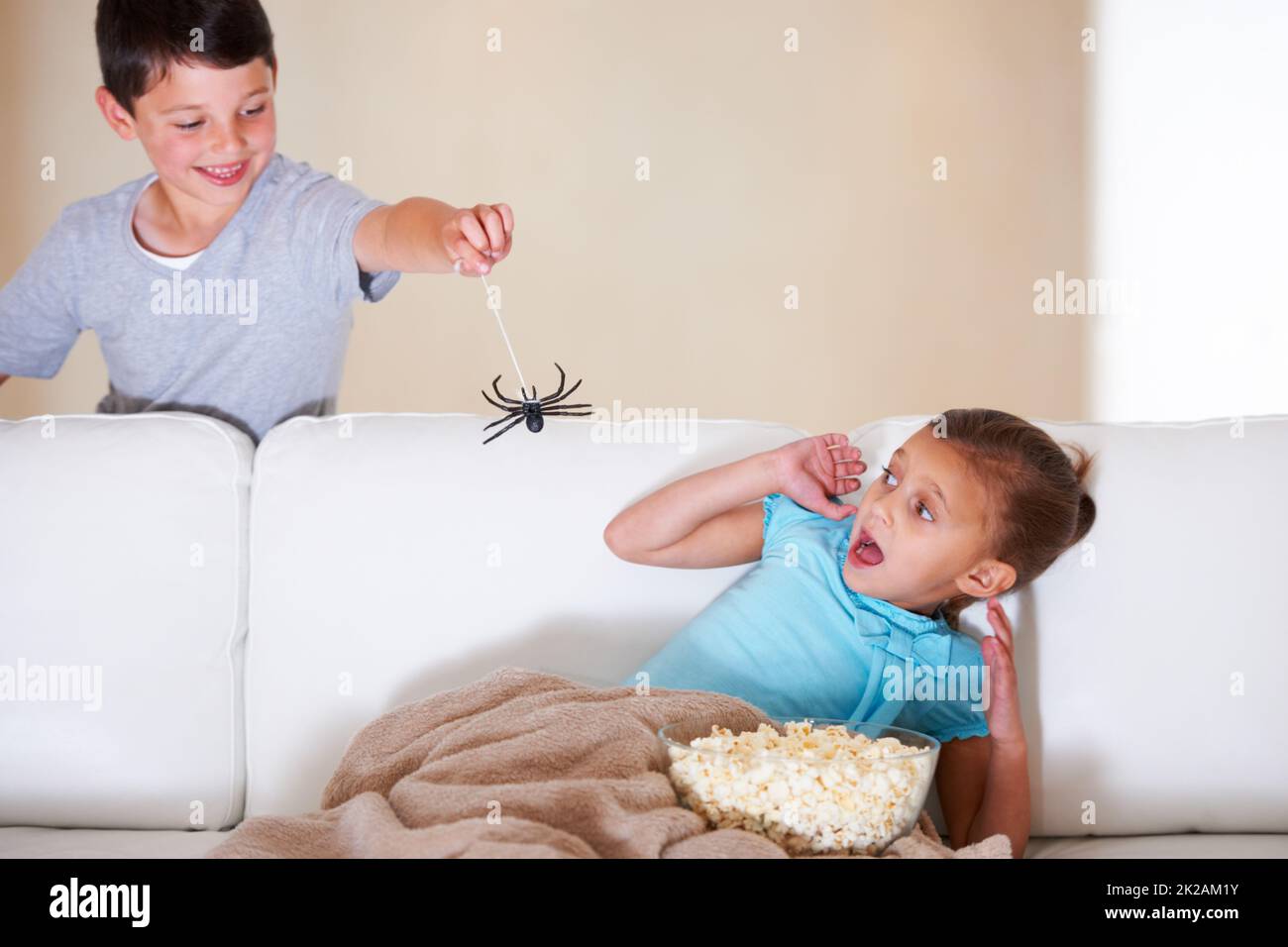 Gotcha. Un jeune garçon espiègle craquant sa petite sœur à Halloween avec une araignée en caoutchouc. Banque D'Images