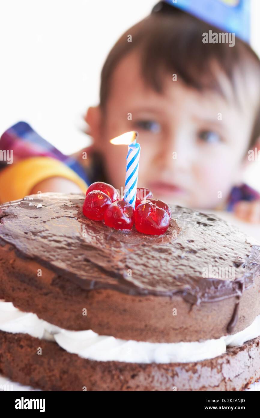 Célébrer une journée spéciale. Un gâteau d'anniversaire avec une bougie avec le garçon d'anniversaire en arrière-plan. Banque D'Images