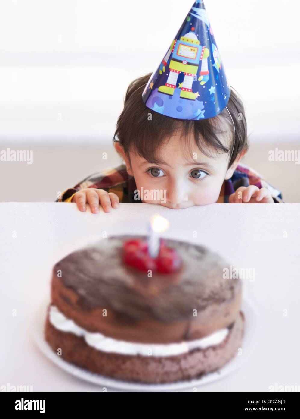 Je veux juste un peu de goût Un petit garçon mignon regardant son gâteau d'anniversaire en anticipation. Banque D'Images
