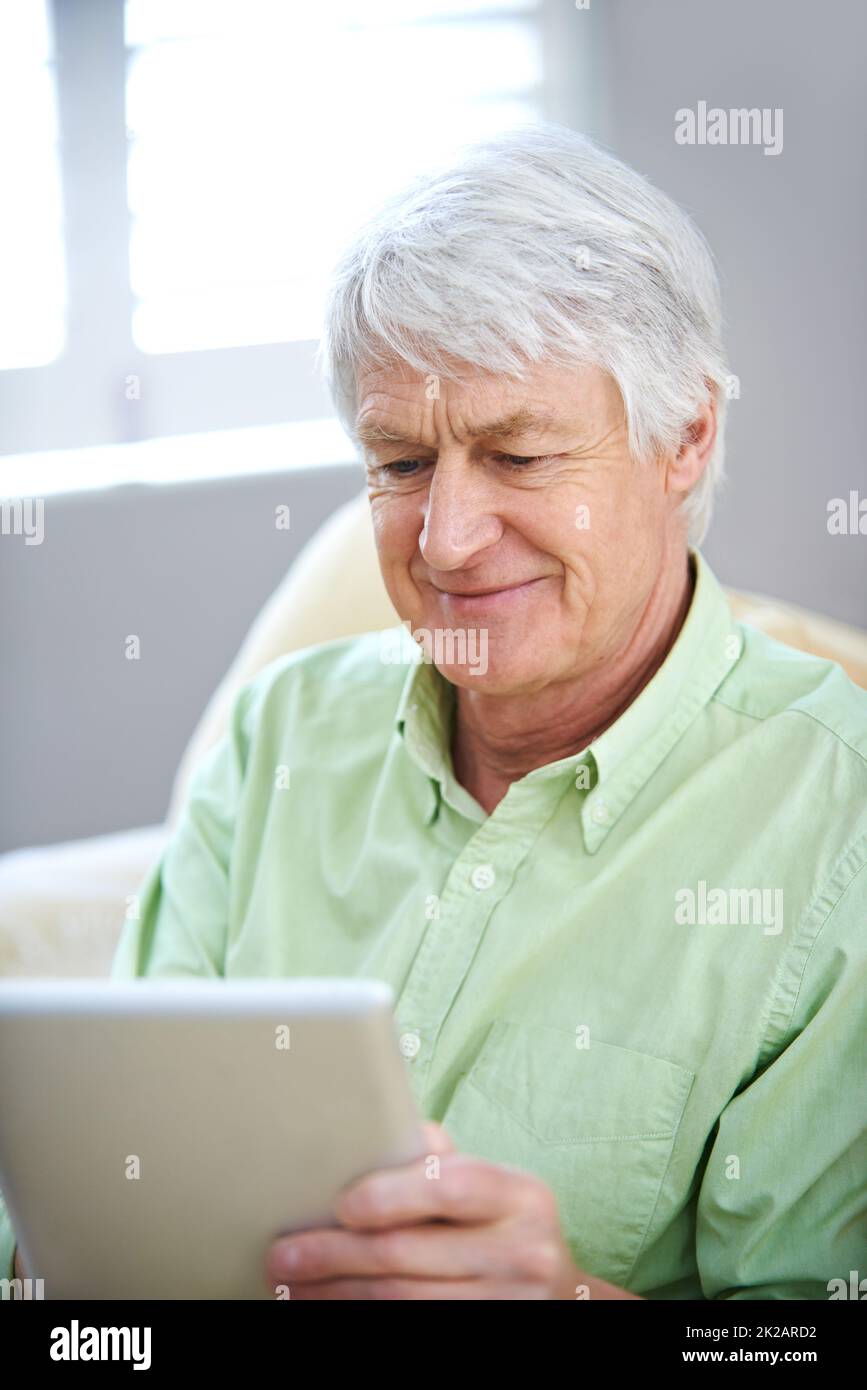 Il y a un tout nouveau monde sur le Web. Un homme âgé utilisant une tablette numérique tout en étant assis sur le canapé à la maison Banque D'Images