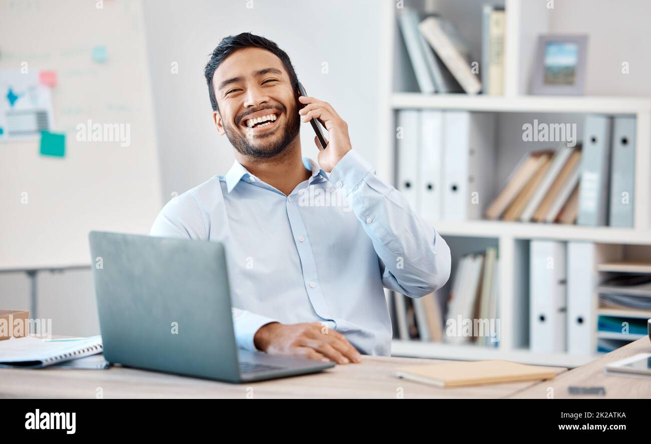 Un homme d'affaires heureux lors d'un appel téléphonique tout en travaillant sur un ordinateur portable au bureau de son bureau moderne. Le directeur de l'entreprise, professionnel et professionnel riant Banque D'Images