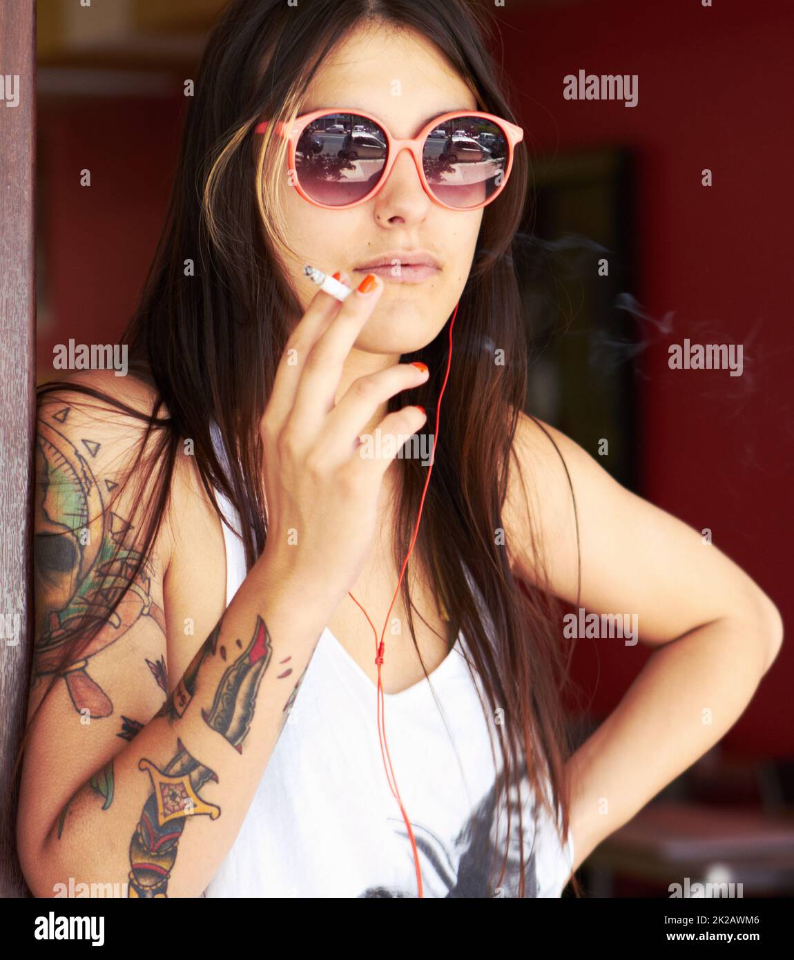 Rebel à cœur. Photo d'une belle jeune femme tatouée fumant une cigarette tout en écoutant de la musique. Banque D'Images