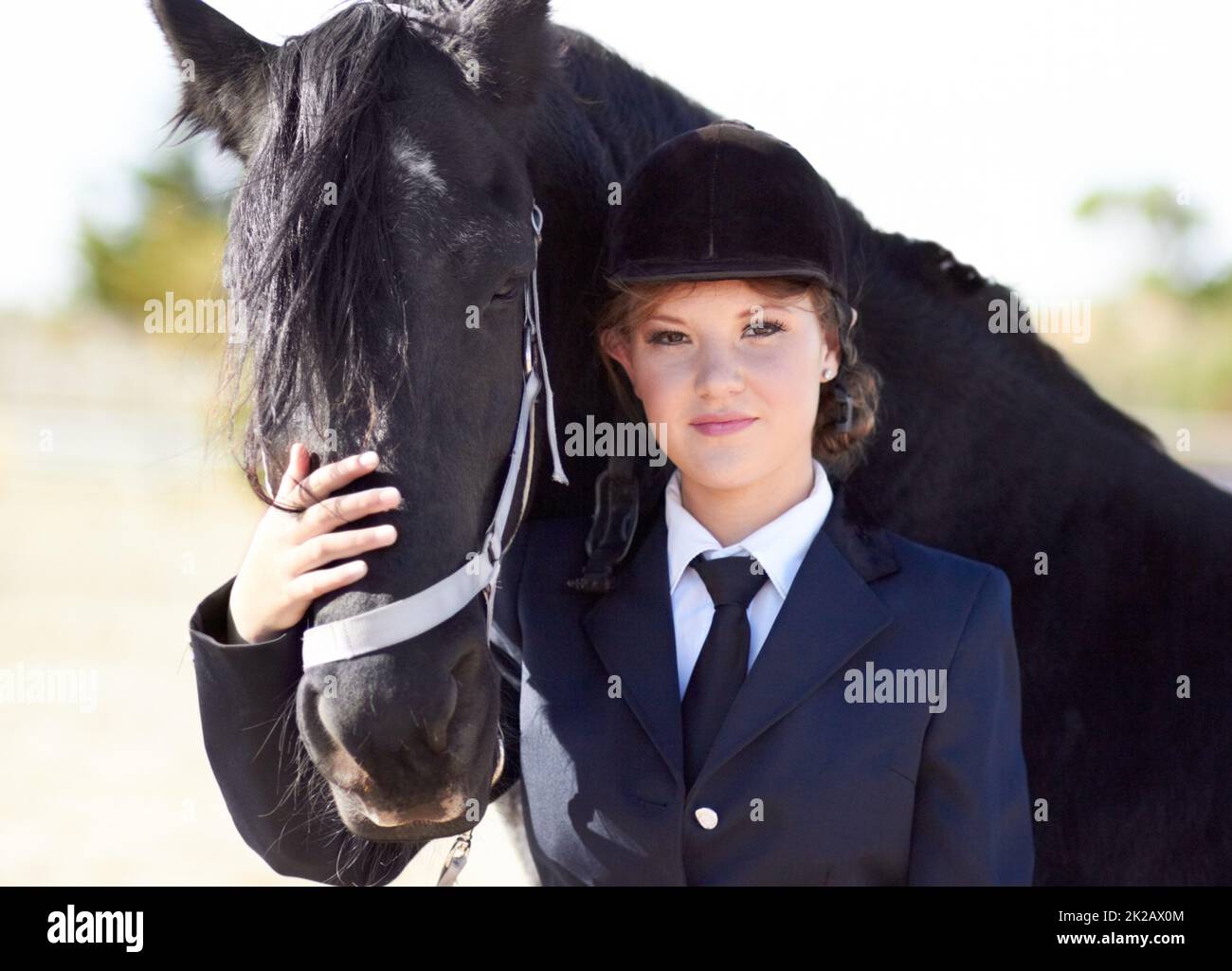 Cheval et cavalier partagent un lien fort Portrait d'une jeune femme pilote qui lui fait face à ses chevaux et qui sourit fièrement à l'appareil photo. Banque D'Images