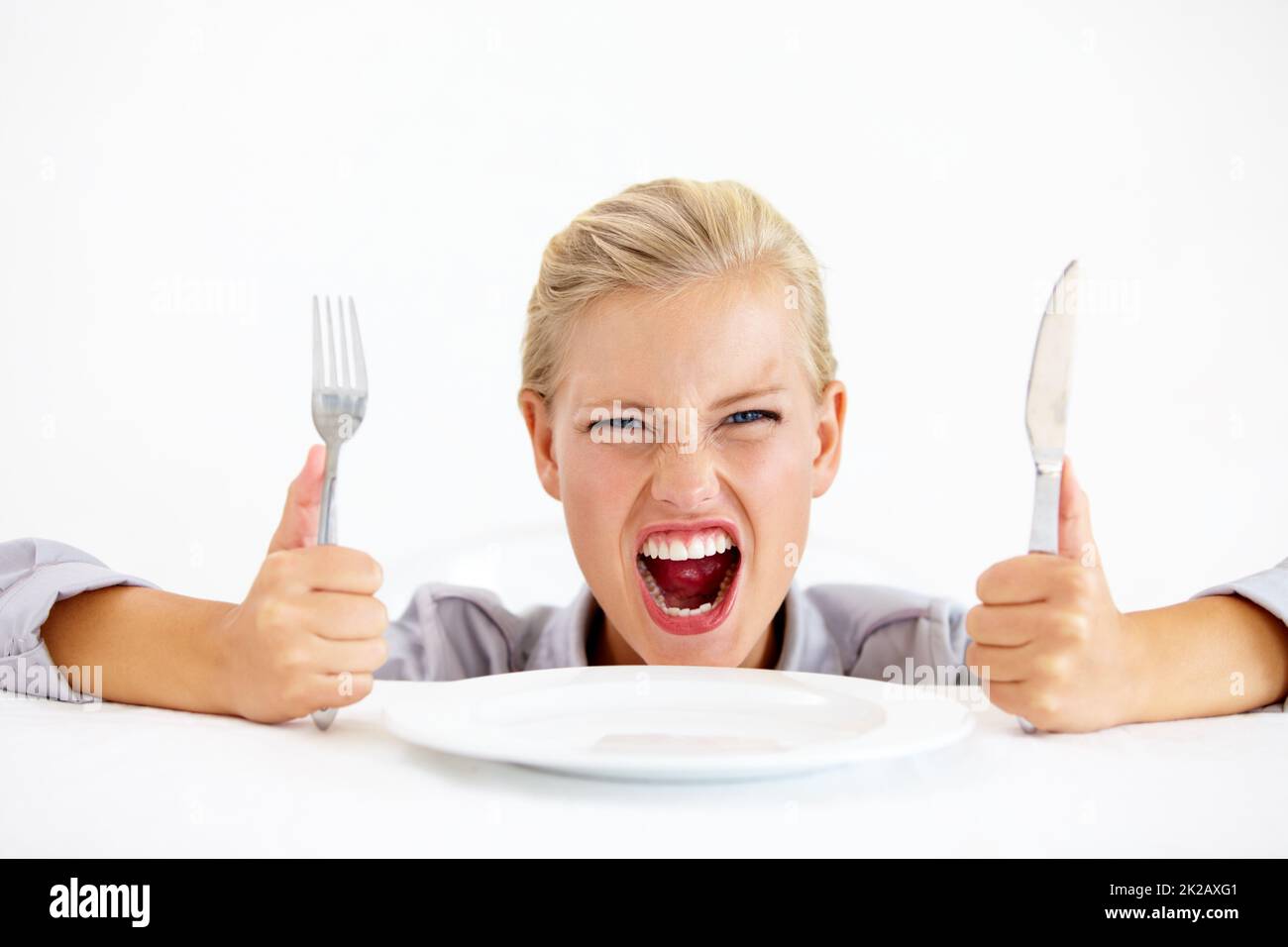 C’est ridicule et affamé. Une jeune femme furieuse assise devant une assiette vide tout en tenant son couteau et sa fourchette. Banque D'Images
