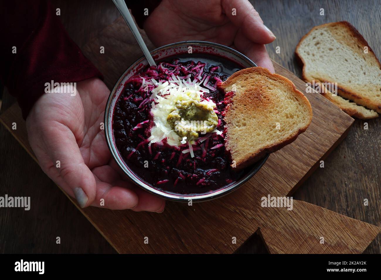 Mains de femmes tenant une assiette de soupe de légumes avec betterave, fromage, crème sure et pain sur fond de bois arustic Banque D'Images