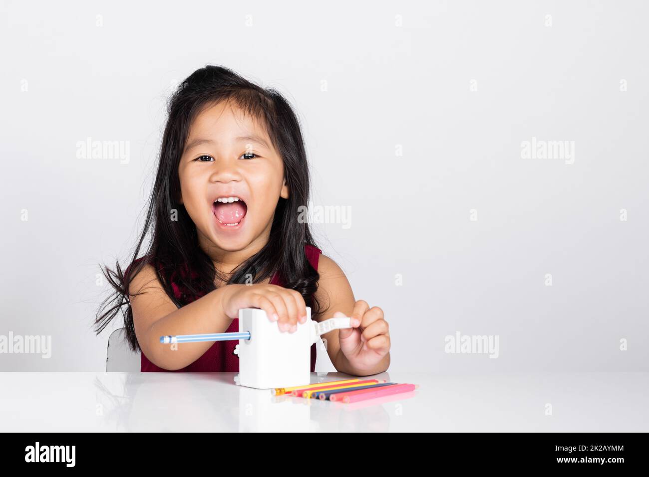 Petite petite petite fille mignonne 3-4 ans sourire à l'aide d'un taille-crayon tout en faisant des devoirs en studio photo isolée Banque D'Images