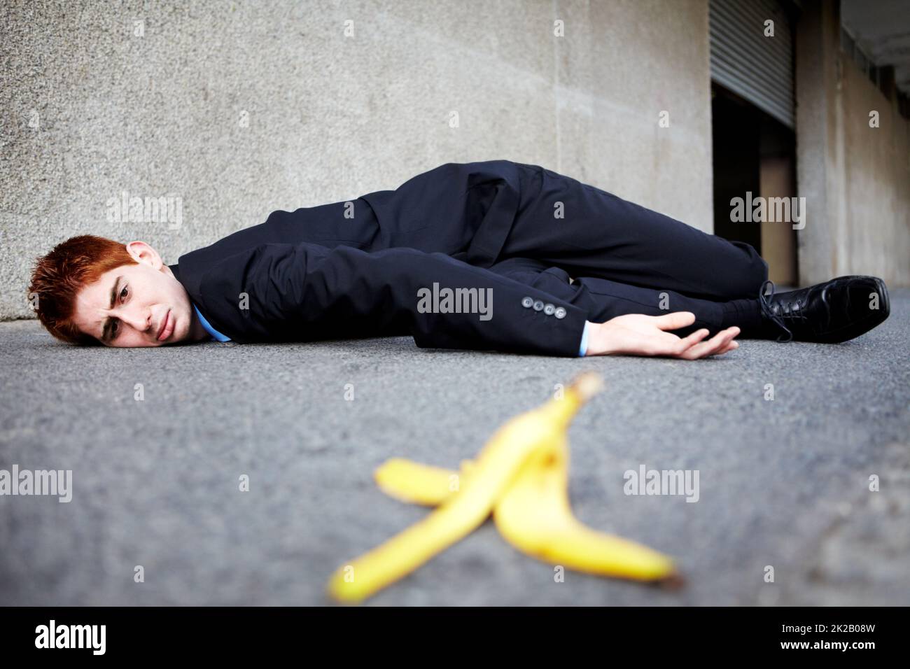 Parfois, les peaux de bananes sont inévitables. Un jeune homme allongé sur le sol après avoir glissé sur une peau de banane. Banque D'Images