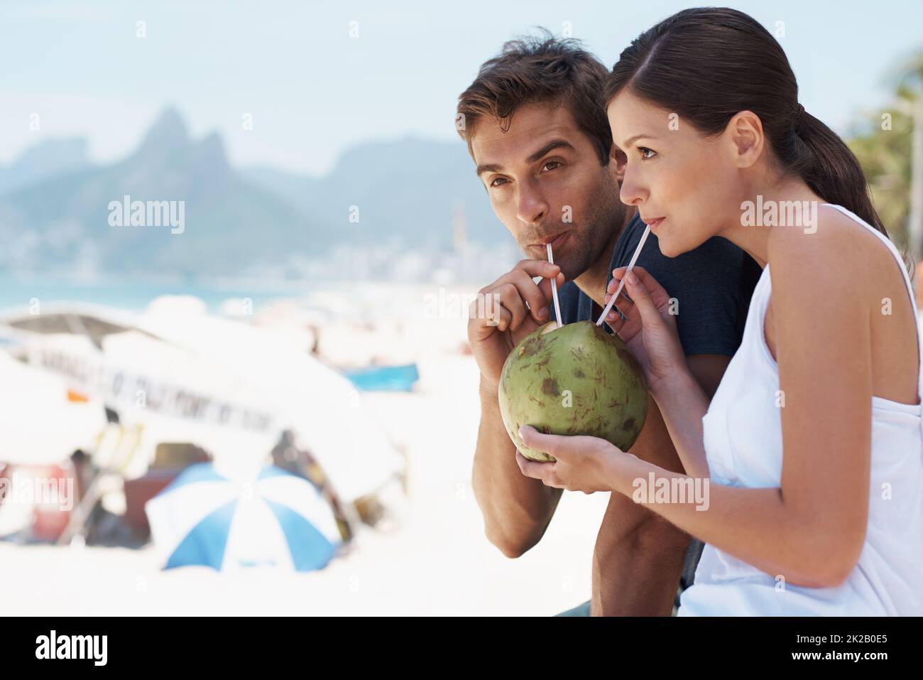 Profiter de quelque chose de nouveau avec la personne que j'aime. Un jeune couple qui apprécie un verre à la noix de coco tout en appréciant une journée à la plage. Banque D'Images