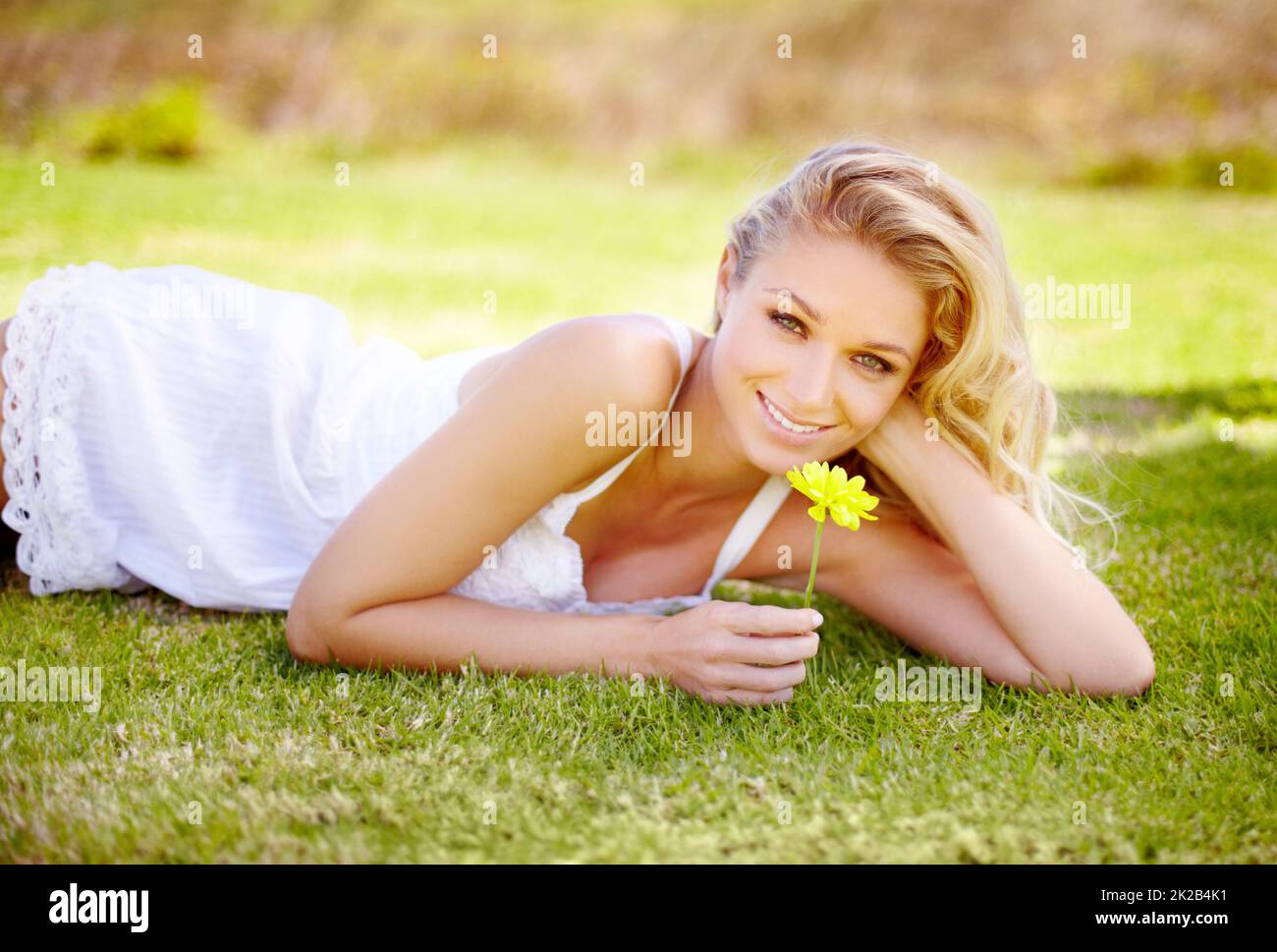L'été est sa saison préférée. Superbe femme blonde détendue dans son jardin et tenant une Marguerite jaune. Banque D'Images