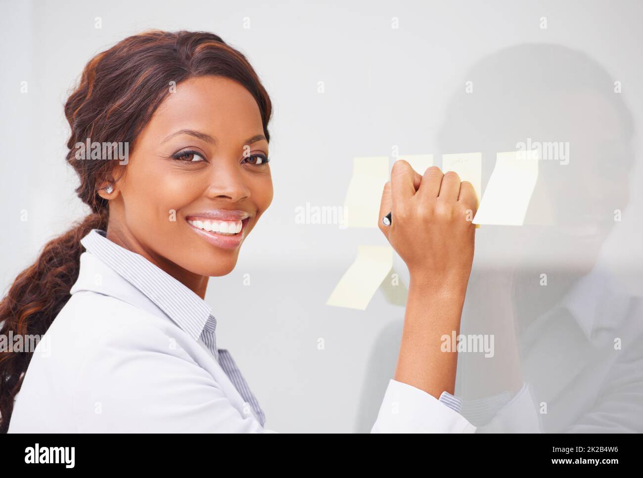 Tri de ses pensées. Une femme afro-américaine qui colle des post-its sur un mur de verre. Banque D'Images
