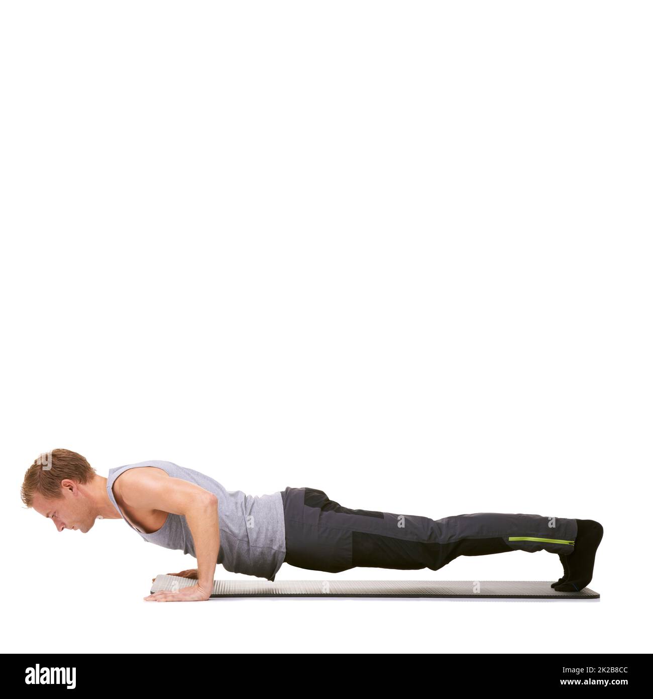 Déterminé à atteindre ses objectifs de forme physique. Un jeune homme en forme faisant des push-up sur son tapis d'exercice tout en étant isolé sur blanc. Banque D'Images