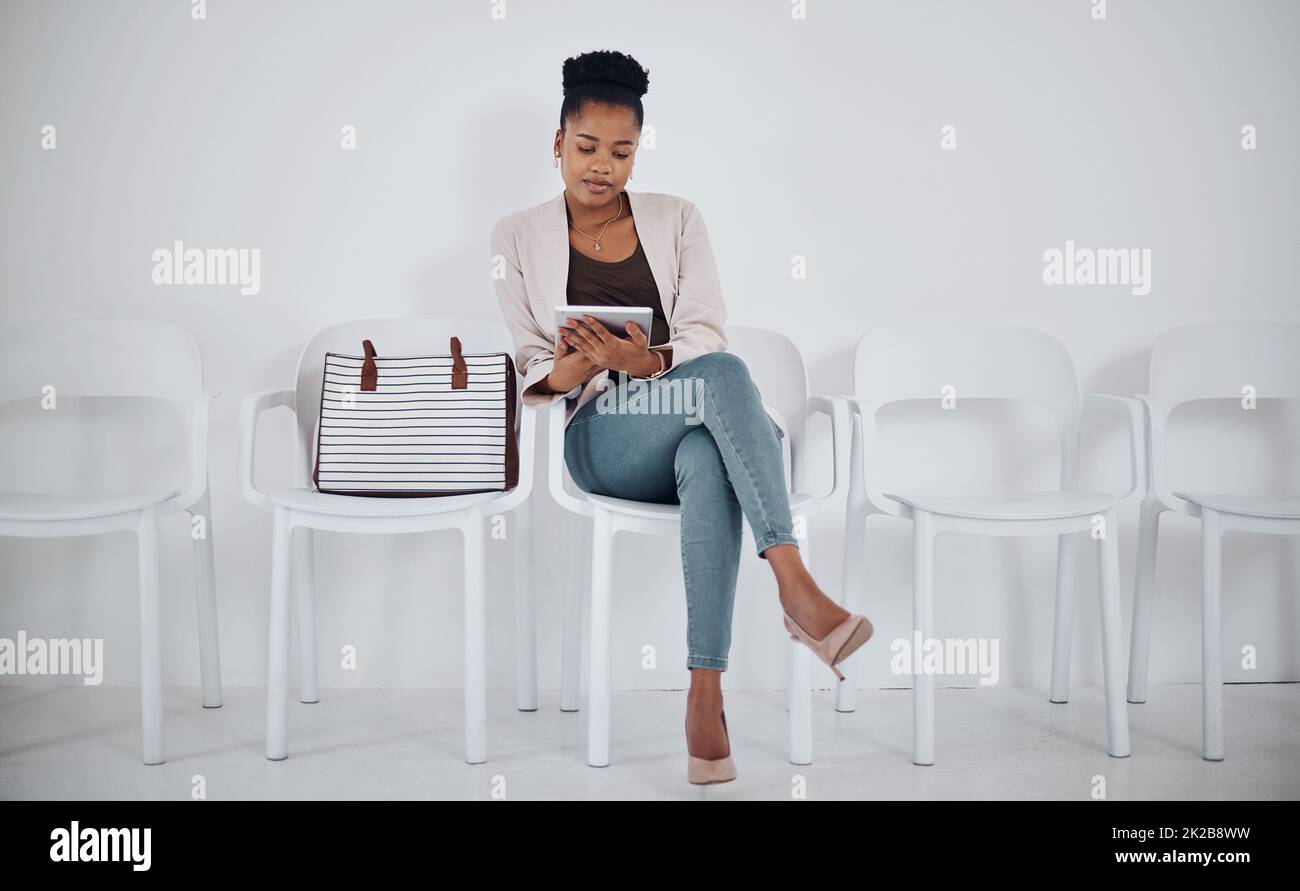 La technologie permet de passer le temps. Prise de vue d'une jeune femme d'affaires utilisant une tablette numérique tout en étant assise dans une ligne sur un fond blanc. Banque D'Images