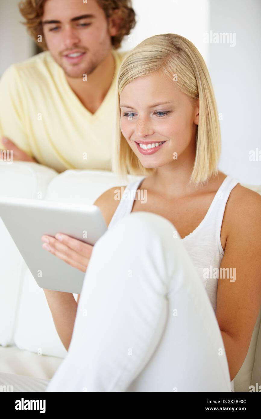 Utilisation de la technologie d'écran tactile. Une belle jeune femme utilisant une tablette comme son petit ami montres de par-dessus son épaule. Banque D'Images