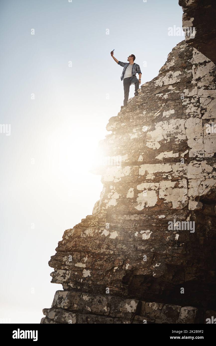 Prendre une photo en haute altitude. Photo d'un jeune homme qui prend des photos en se tenant sur le bord d'une falaise de montagne. Banque D'Images
