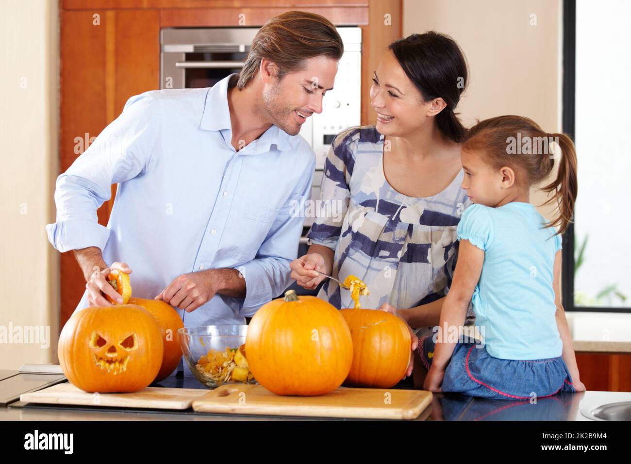 Préparer la citrouille pour Halloween. Une jeune mère et un père debout avec leur jeune fille dans une cuisine préparant Jack Olanternes pour Halloween. Banque D'Images