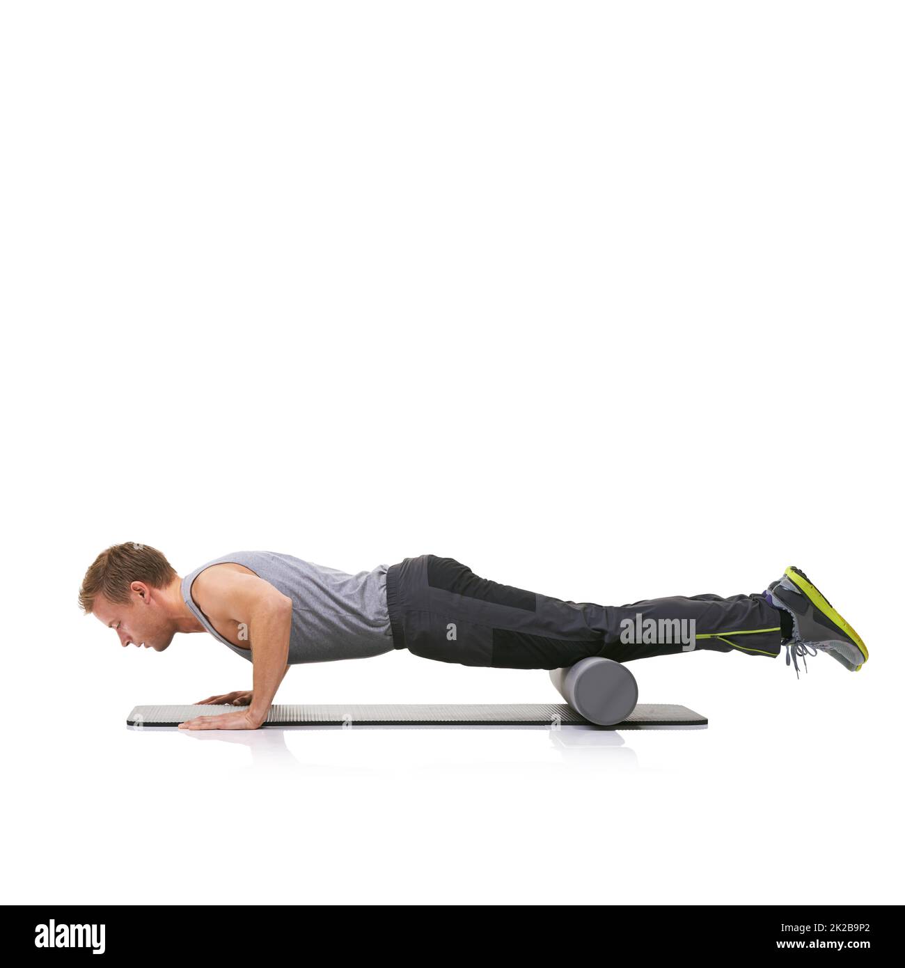 Améliorer sa force et sa flexibilité. Un jeune homme qui fait des push-up sur son tapis d'exercice avec ses jambes soulevées par un rouleau en mousse. Banque D'Images