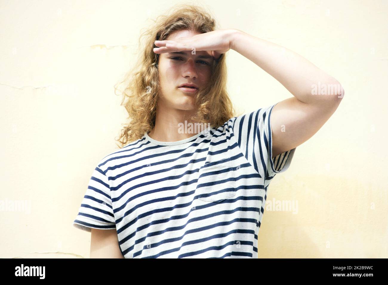 À l'avenir. Jeune homme avec des cheveux longs et bouclés et un sens décontracté du style vous regardant. Banque D'Images