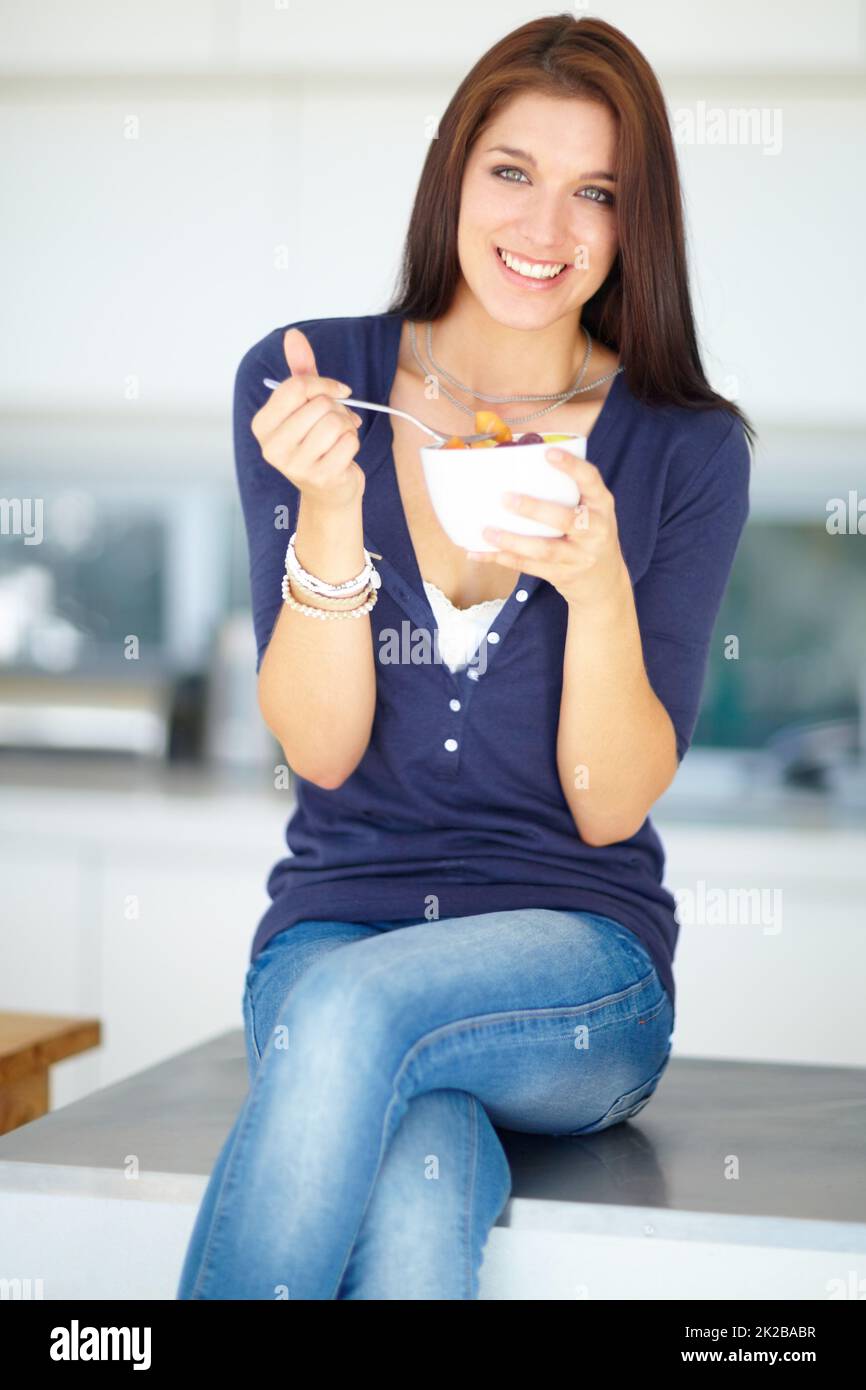 Dégustez un en-cas sain. Portrait d'une jeune femme souriante mangeant une salade de fruits saine pour le déjeuner. Banque D'Images
