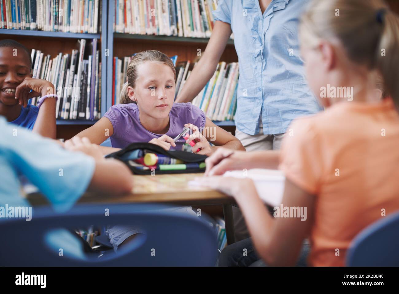 Se concentrer sur son travail. Une jeune fille assise à la bibliothèque avec ses camarades de classe et son professeur. Banque D'Images