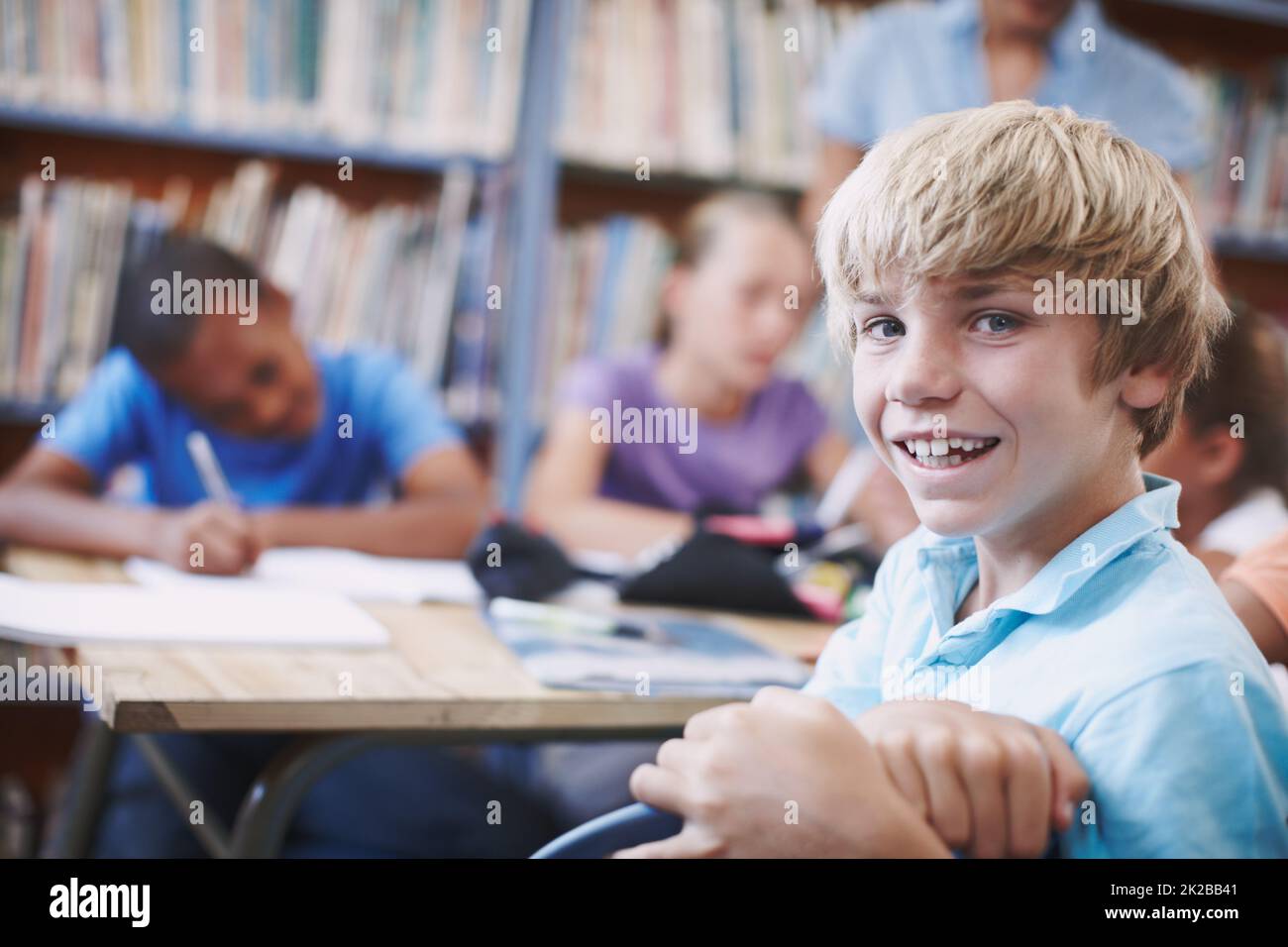 Je vous fait tellement d'amis. Un jeune garçon excité assis dans la bibliothèque avec ses camarades de classe. Banque D'Images