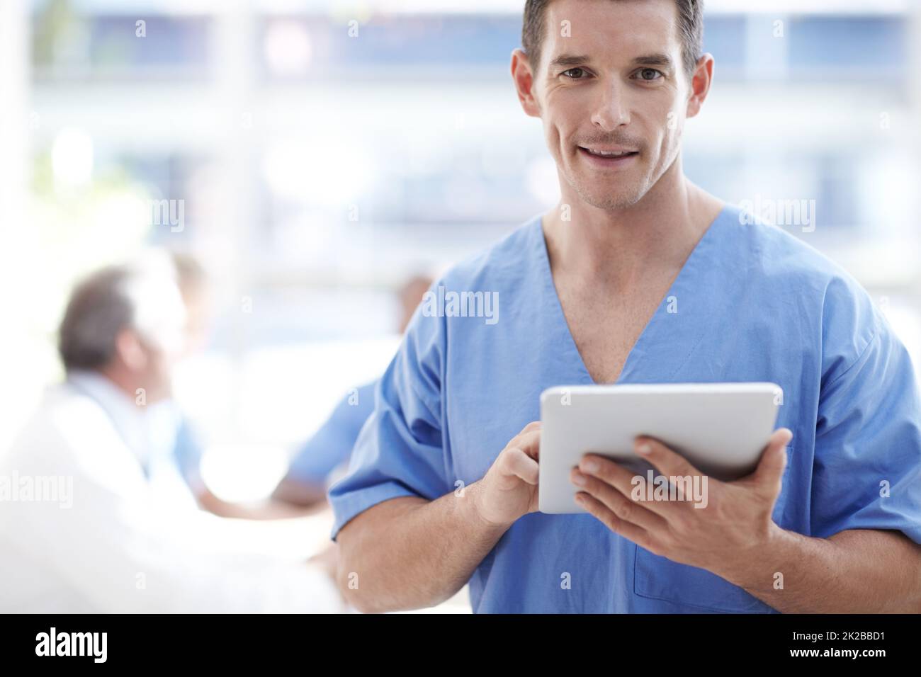 Médecin numérique. Un professionnel de la santé travaillant sur un pavé tactile avec des collègues assis en arrière-plan. Banque D'Images