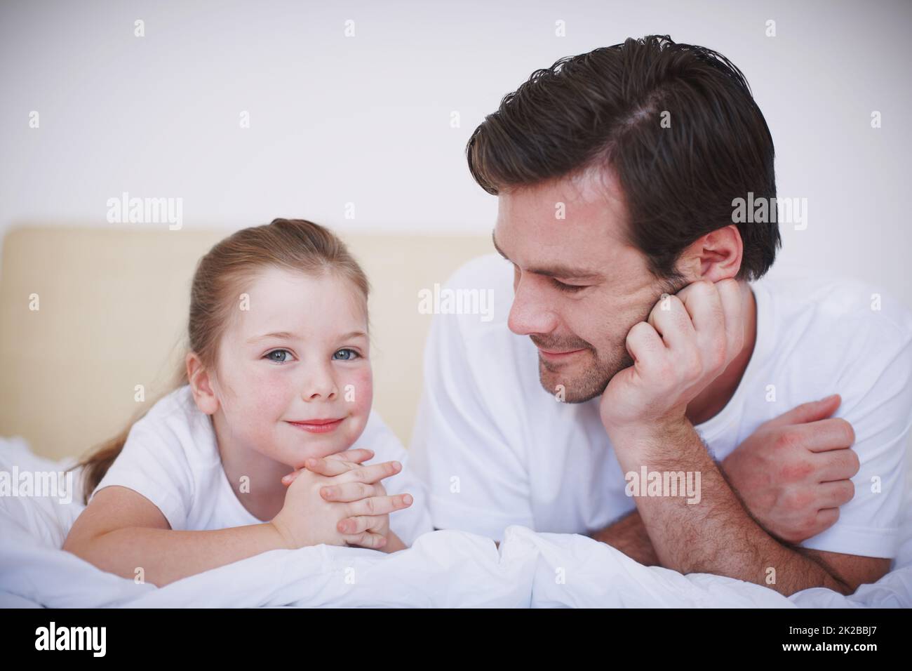 Il fera quoi que ce soit pour sa petite fille. Un père et sa jeune fille allongé côte à côte sur un lit. Banque D'Images