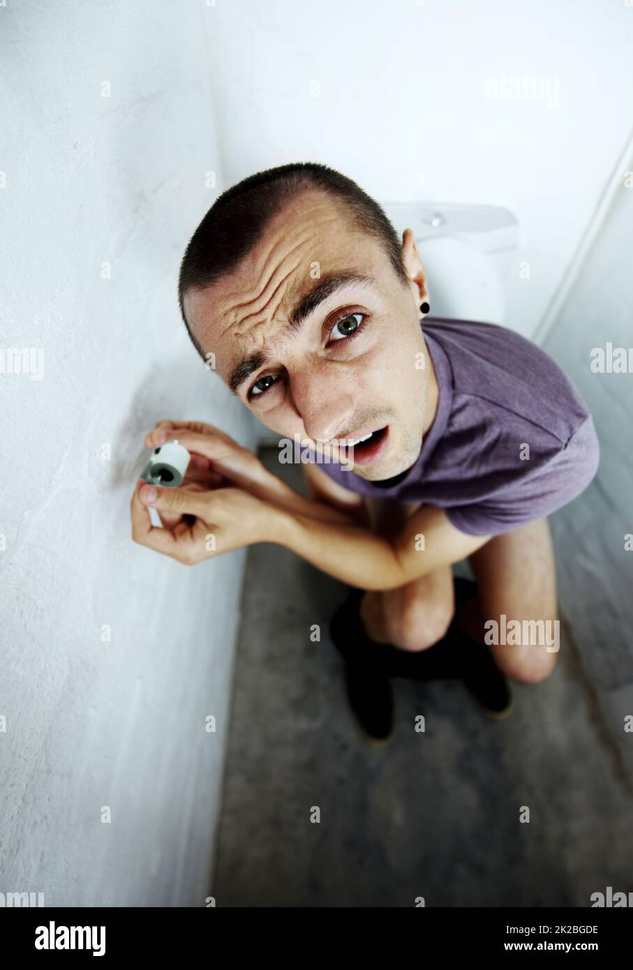Sensation d'exposition. Un jeune homme s'est coincé dans une toilette essayant d'atteindre un petit rouleau de papier toilette. Banque D'Images