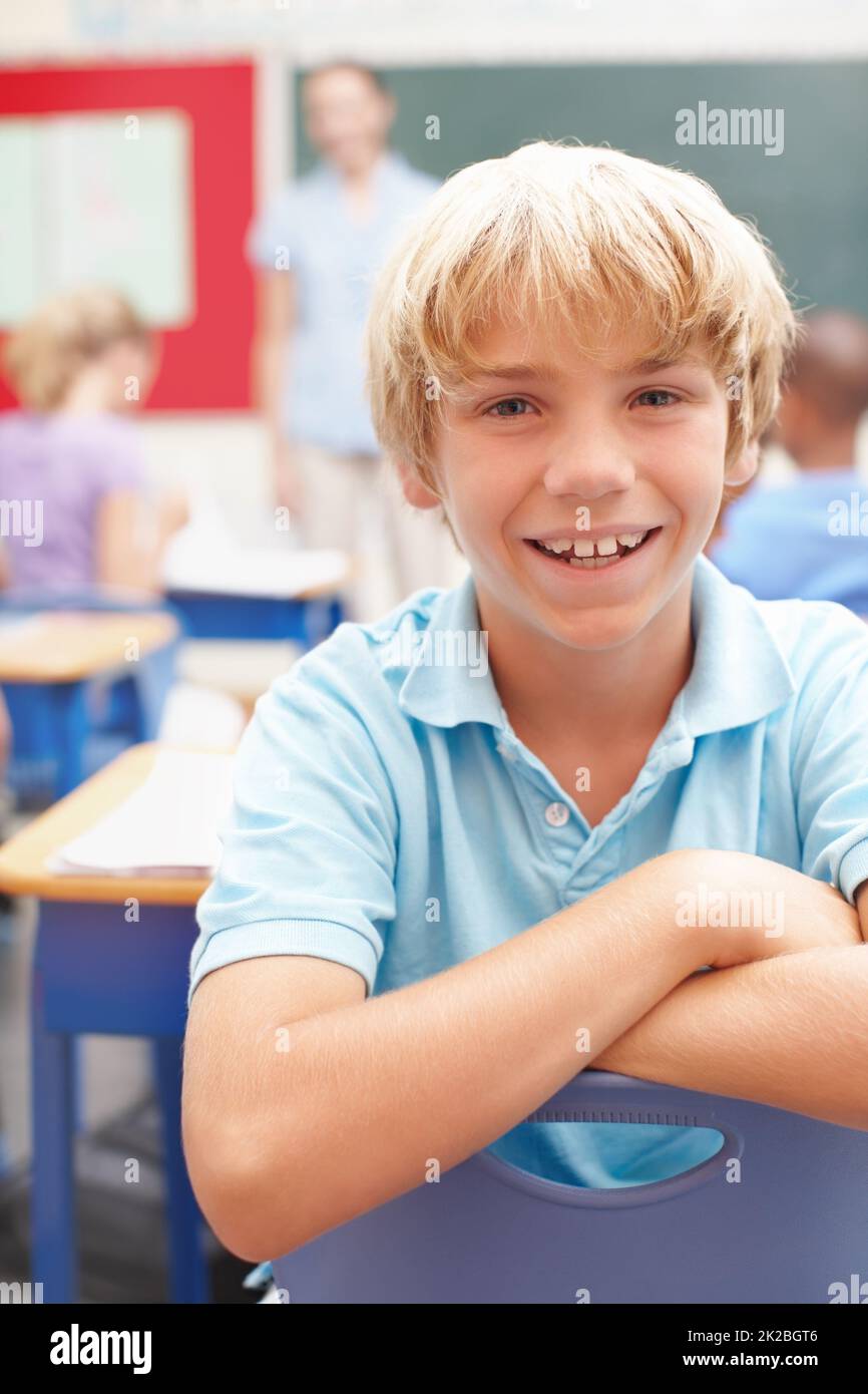 Il aime la classe. Portrait d'un jeune garçon blond mignon assis à un bureau en classe. Banque D'Images