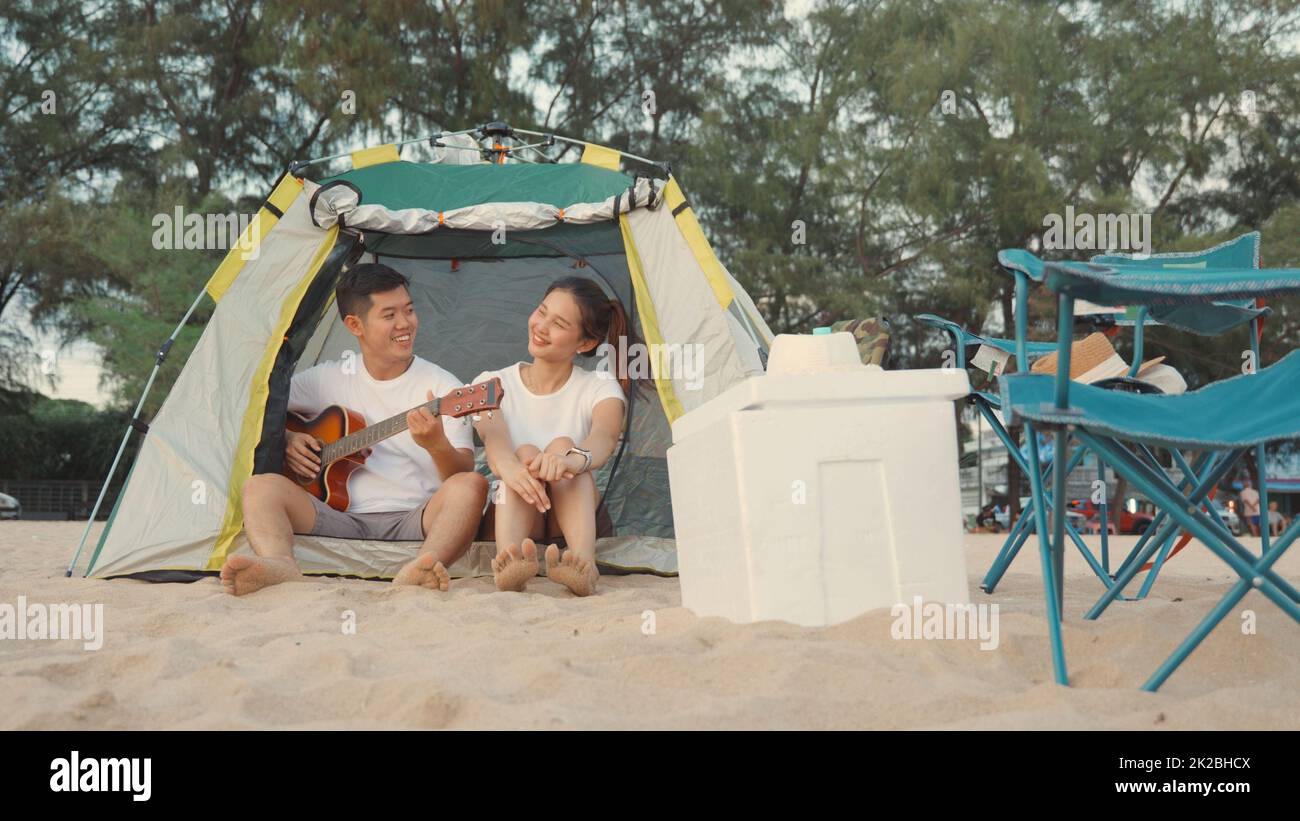 Jeune couple aimant joli en camp jouant de la guitare tout en s'asseyant à la tente de camping sur la plage Banque D'Images