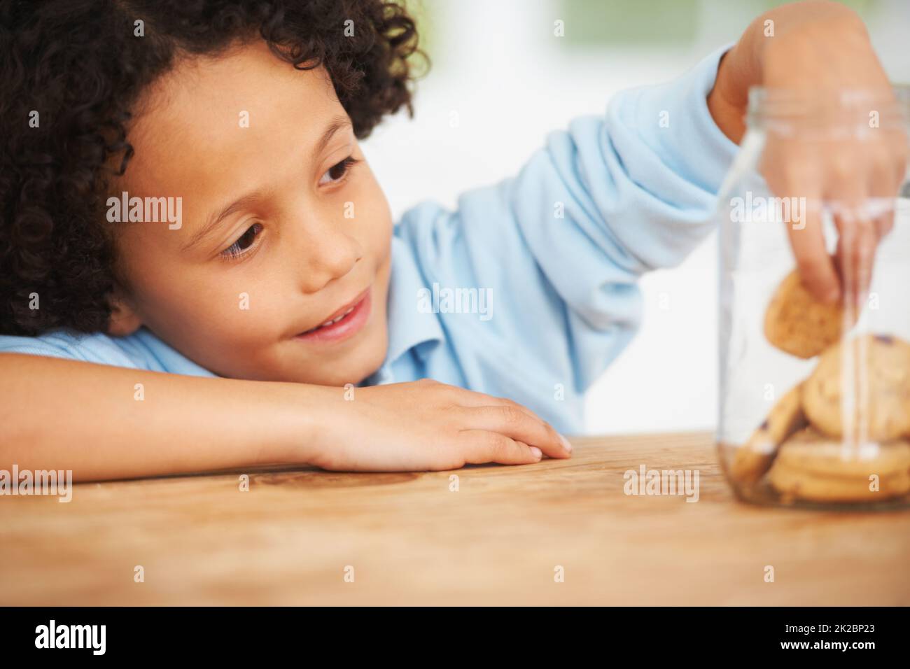 MMM, tellement de cookies juste pour moi. Un jeune garçon mignon saisissant un cookie du pot à biscuits. Banque D'Images