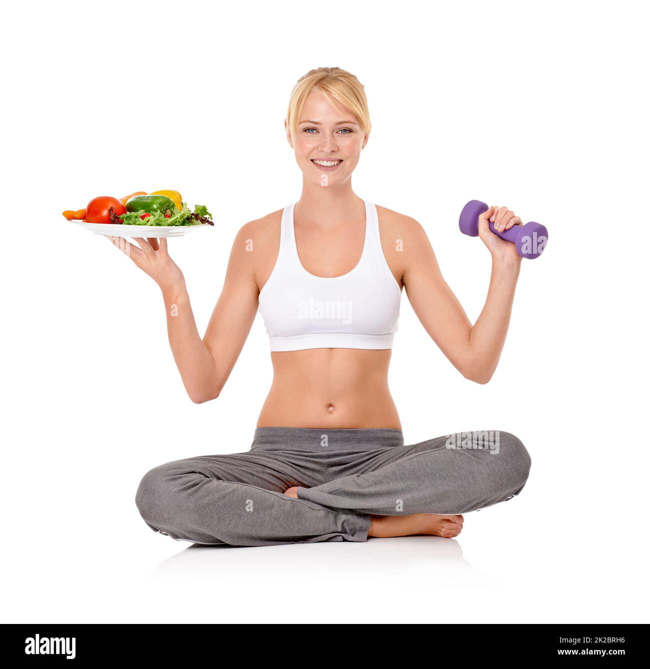 Bonne nourriture et exercice - la combinaison parfaite. Portrait d'une belle jeune femme tenant une salade dans une main et une haltère dans l'autre. Banque D'Images