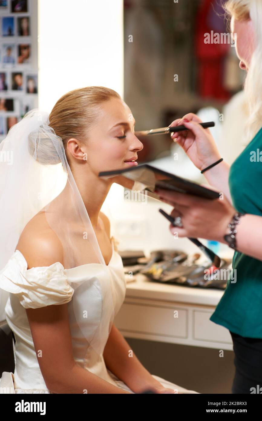 S'assurer qu'elle a l'air parfaite. Un artiste de maquillage appliquant le maquillage à une mariée. Banque D'Images