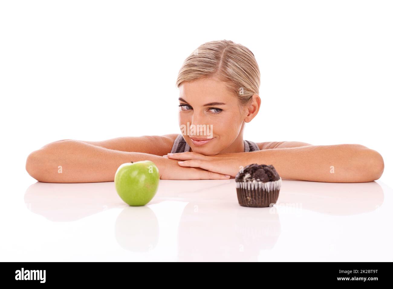 Un choix aussi difficile. Une jolie jeune femme qui fait le choix entre un cupcake ou une pomme. Banque D'Images