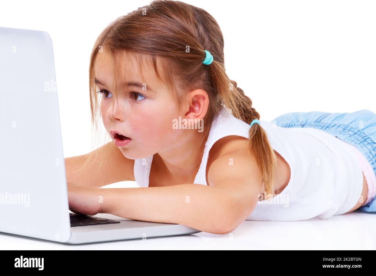 Le cyberespace est un grand endroit pour une petite fille. Une adorable petite fille qui a l'air stupéfait de s'allonger sur un ordinateur portable. Banque D'Images