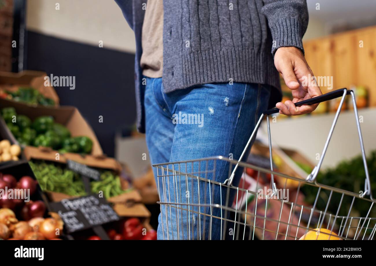 Choisissez les plus frais. Coupe courte d'un jeune homme qui descend dans une allée d'épicerie et qui porte un panier contenant de la nourriture. Banque D'Images