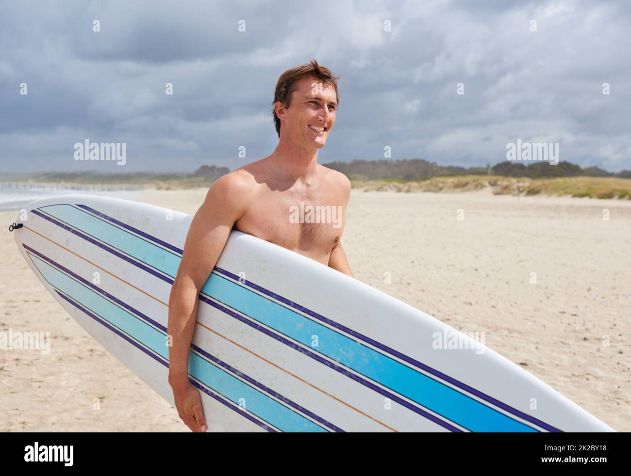 Pour surfer. Un jeune homme tenant sa planche de surf à la plage. Banque D'Images
