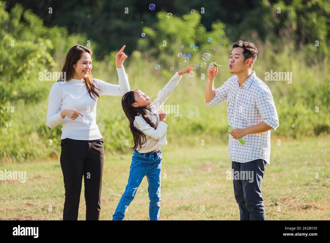 La mère asiatique, le père et la petite fille qui s'amusent ensemble jouent des bulles de savon soufflantes dans le parc Banque D'Images