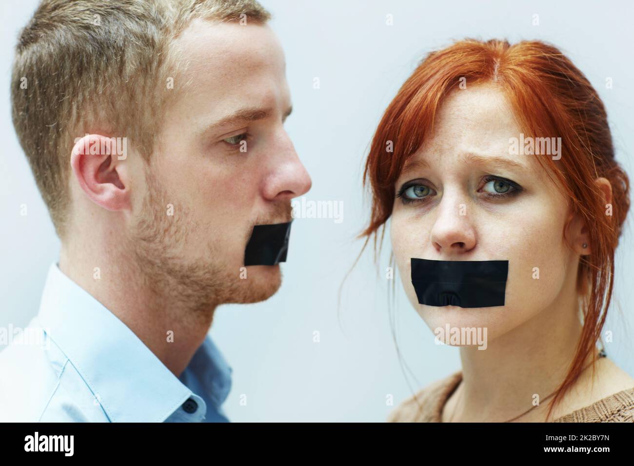 La voix a été réduite au silence. Un jeune couple a l'air triste avec la bande sur leur bouche. Banque D'Images