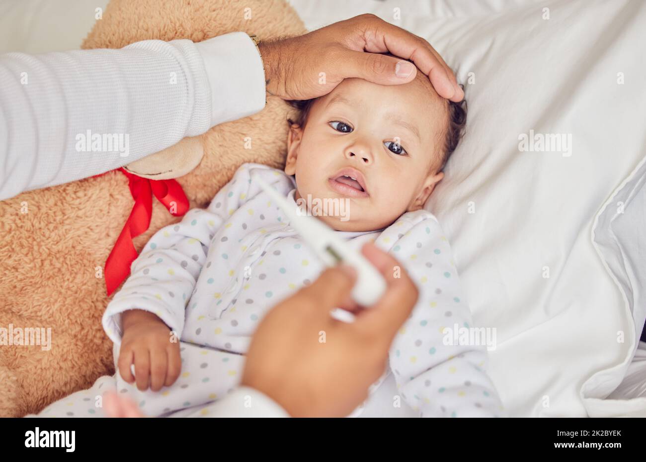 Bébé, malade avec du covid et de la fièvre avec un thermomètre d'un parent d'un enfant malade dans le lit de la chambre de leur maison. Main, front et soins de santé Banque D'Images