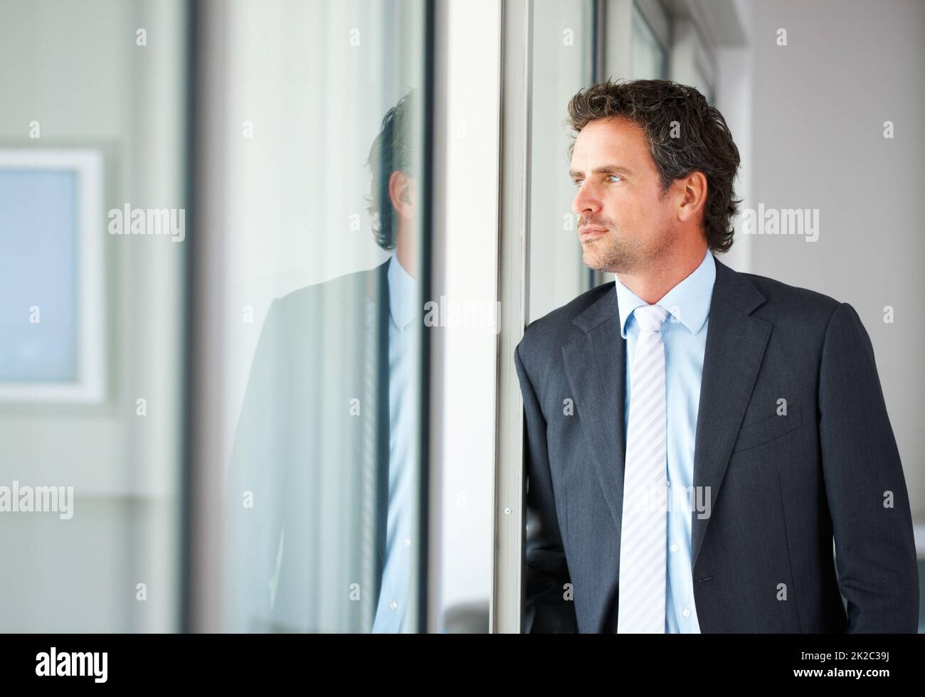 Homme d'affaires regardant par la porte. Un homme d'affaires élégant d'âge moyen qui regarde par une porte vitrée. Banque D'Images