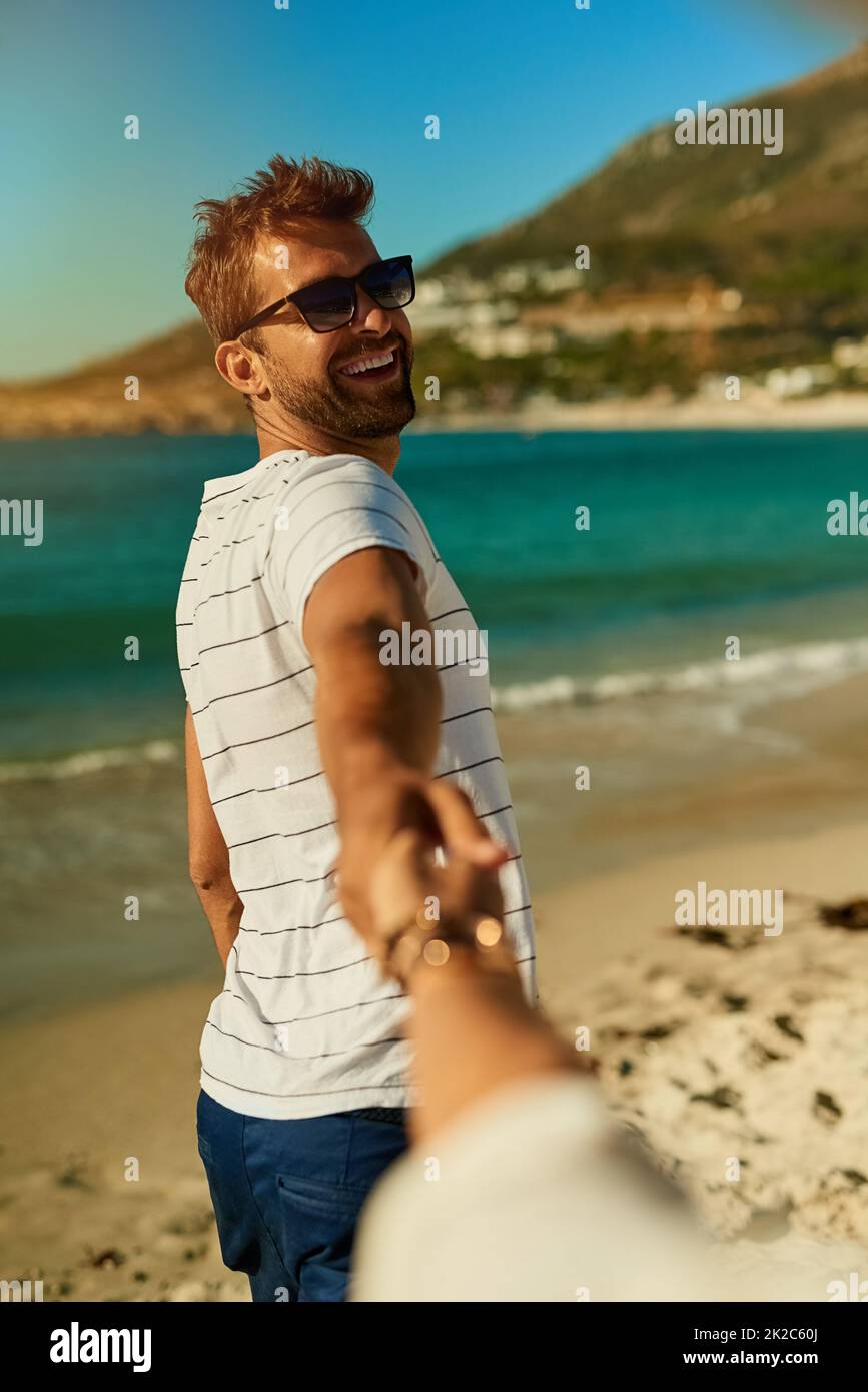 Allons là où le soleil brille tout le temps. Photo d'un jeune homme tenant la main de ses amies et menant le chemin à la plage. Banque D'Images