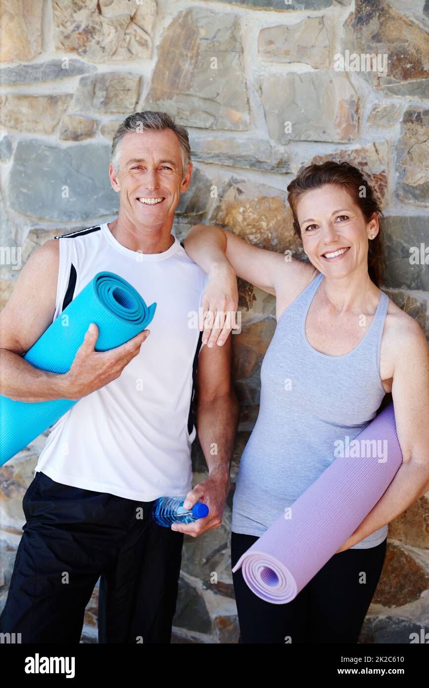 Les passionnés de cours de yoga. Un couple mature tenant son équipement de yoga dehors avec de larges sourires. Banque D'Images